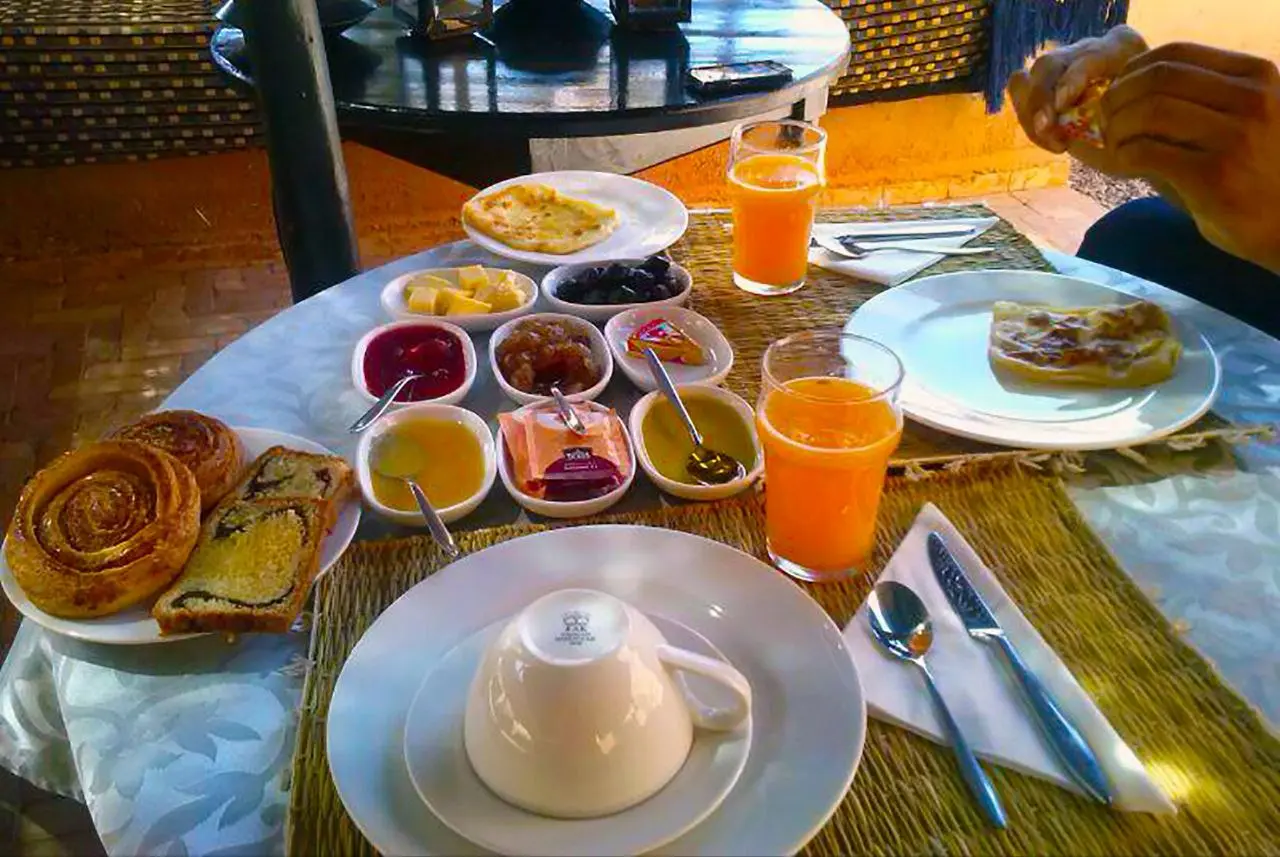 A full breakfast spread with pastries, jams, honey, orange juice, and flatbread on a table.