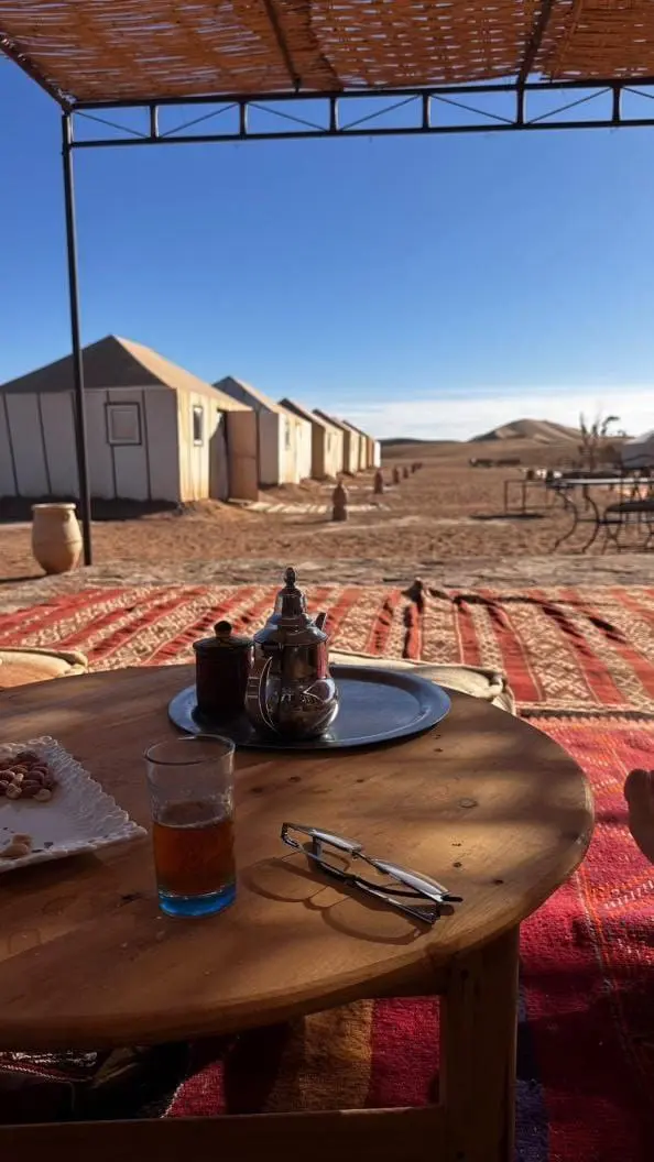 Moroccan tea set on a low wooden table at a desert camp with white tents and sand dunes.