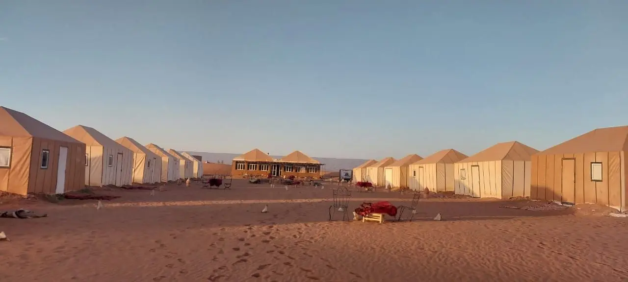 Luxury desert camp with two rows of tan tents and a central building under a clear sky.